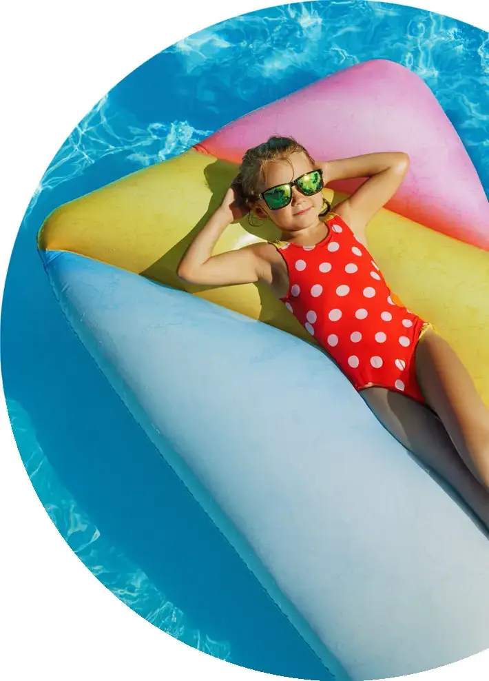 Young girl in red polka dot swimsuit relaxing on colorful inflatable pool float wearing green sunglasses